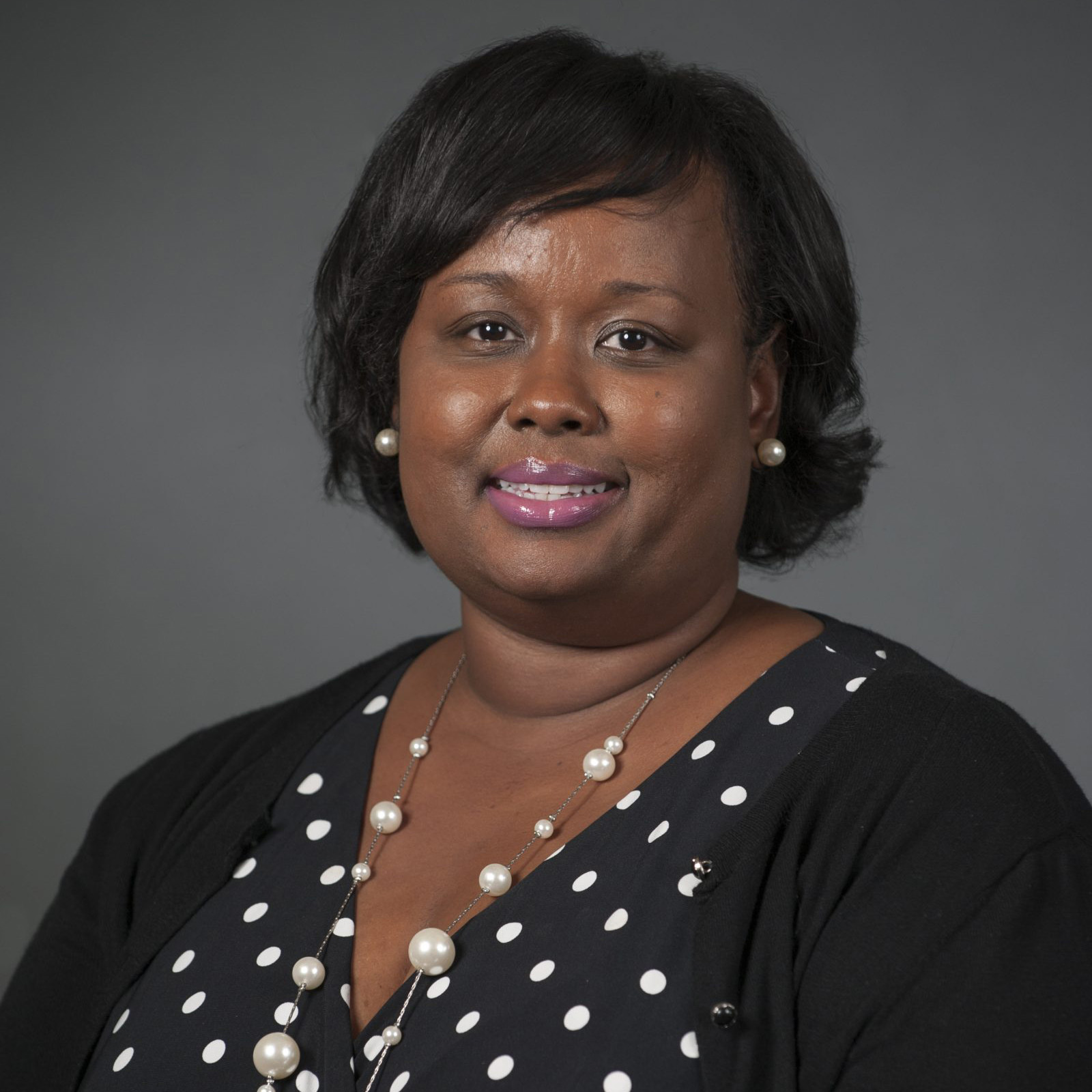 Portrait of Principal Antoinette Powell smiling, wearing a black polka dot blouse, pearl necklace, and earrings against a neutral background.