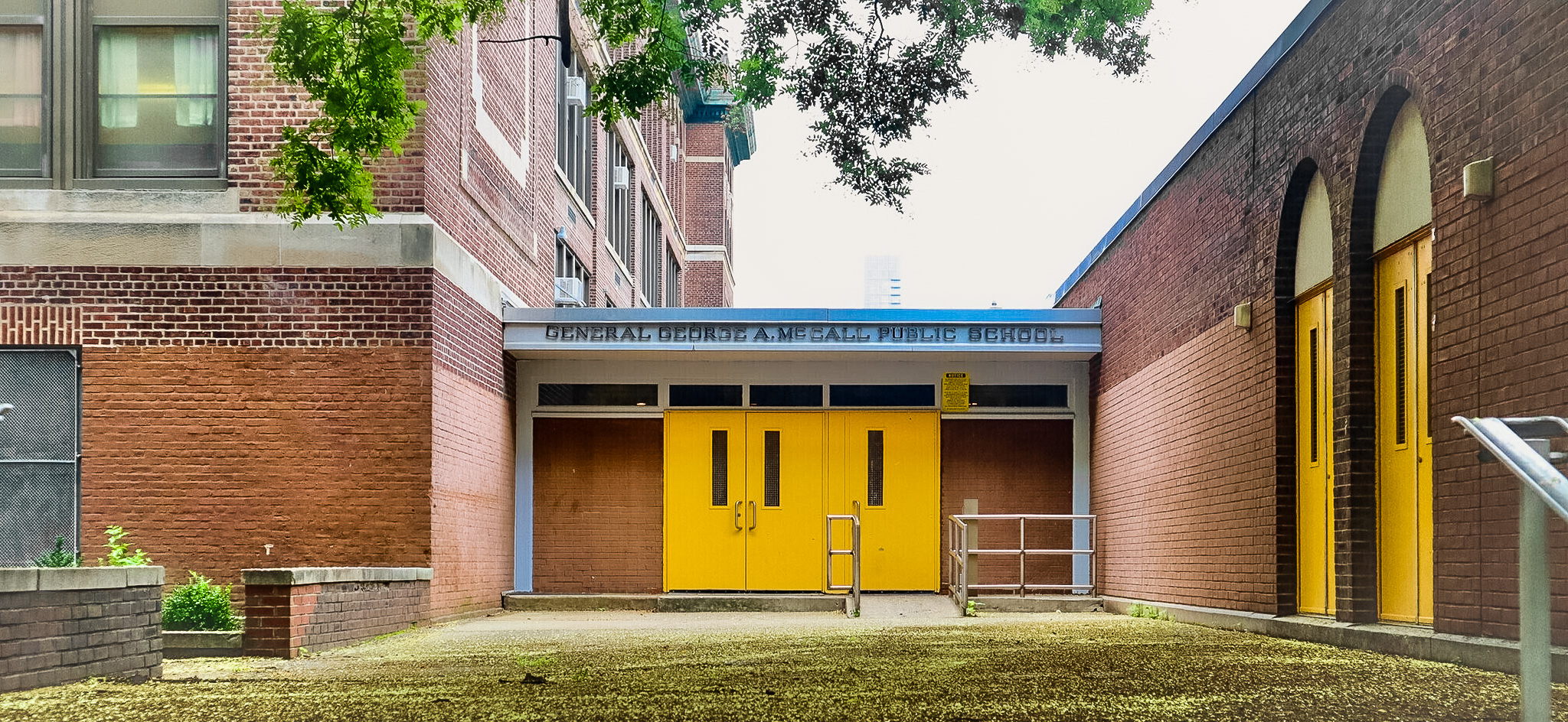 Front entrance of General George A. McCall Public School with bright yellow doors, brick buildings, and the school name displayed above the entryway.